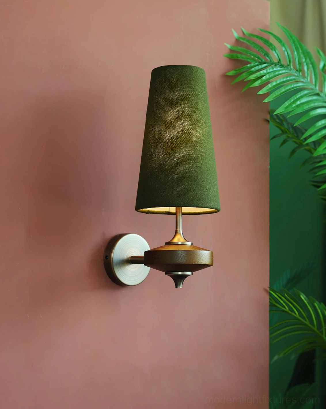 Illuminated Montera wall sconce with dark green shade and light bronze base on terracotta wall with tropical plants