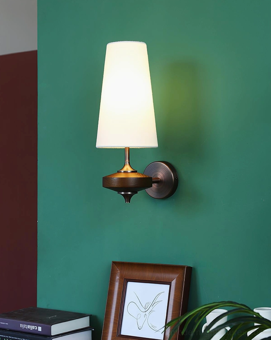 Montera modern wall sconce with off-white conical shade and bronze base, angled view on green accent wall, lit