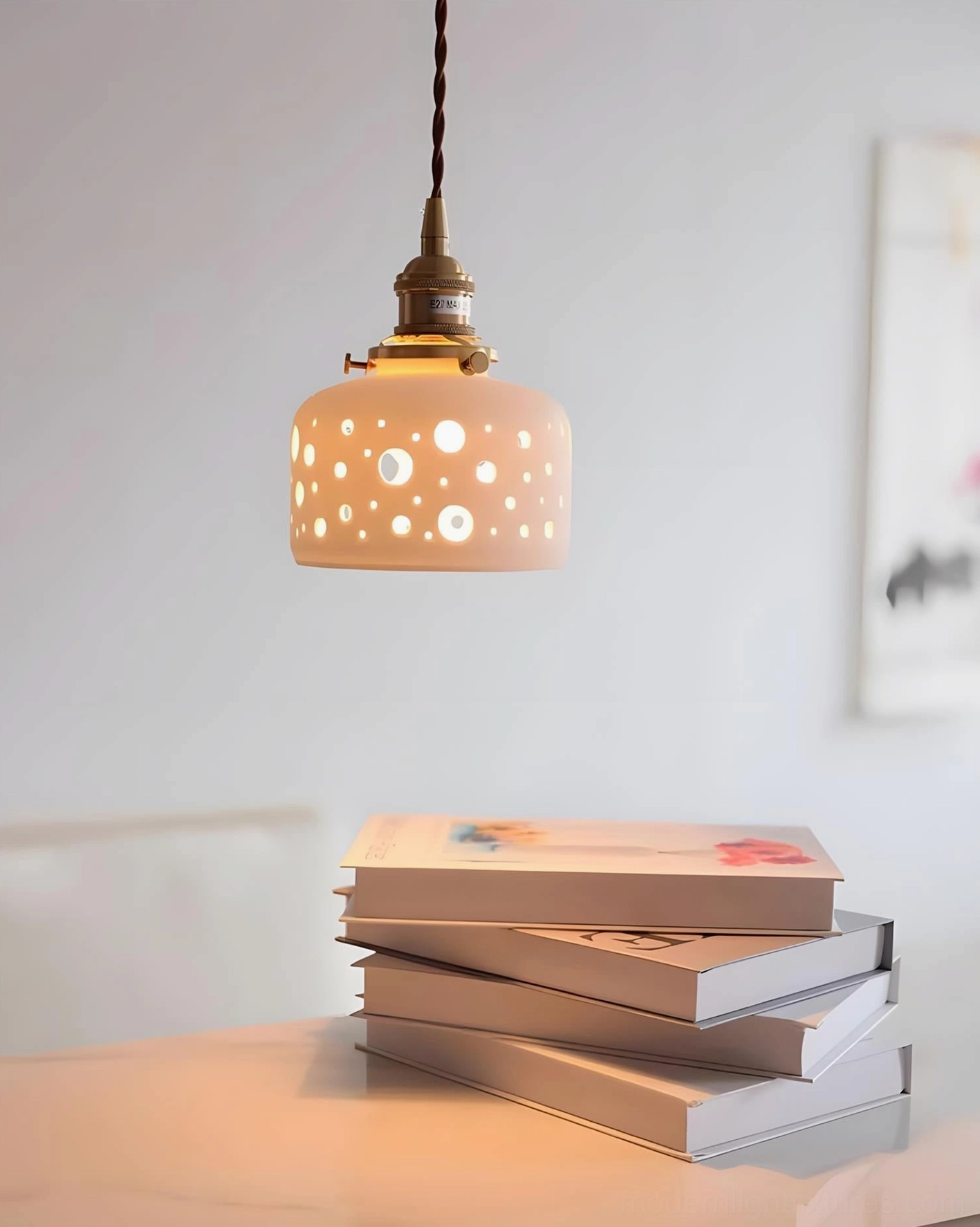 Gentle warm light from Moonveil cutout pendant over stacked books, showcasing decorative shadow casting capability