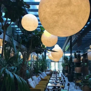 Multiple moon pendant lights hanging in modern dining lounge with green plants and warm ambient light