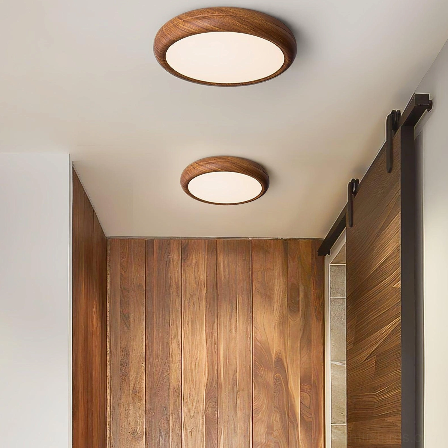 Two different sizes of walnut wood grain ceiling light fixtures installed in hallway with sliding barn door, material continuity