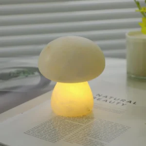 Mushora modern table lamp three-quarter view with warm glow on minimalist bedside table with book and candle