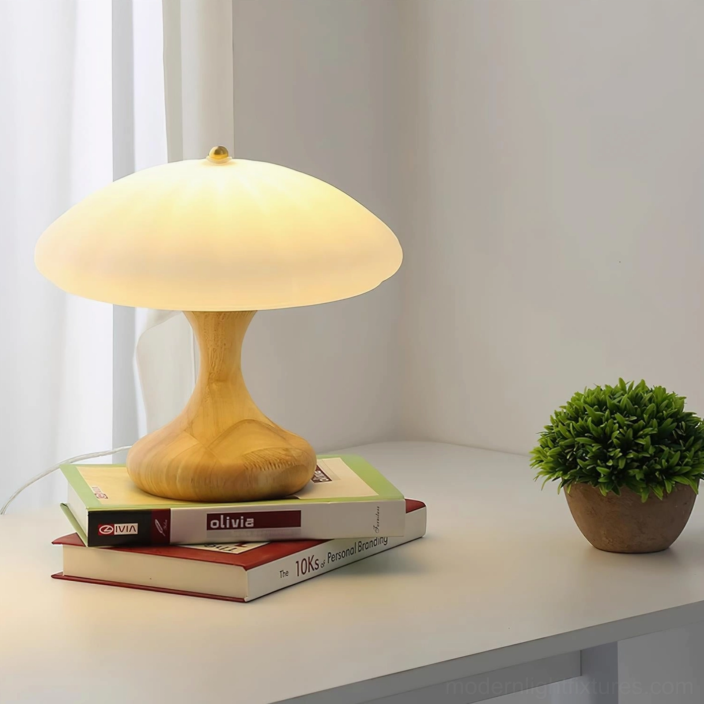 Modern mushroom table lamp positioned on desk with stacked books and potted plant, showcasing light wood base in home interior setting
