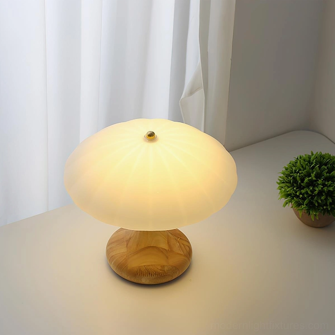 Mushroom table lamp with light wood base and frosted glass shade positioned beside potted plant, sheer curtain backdrop home office scene