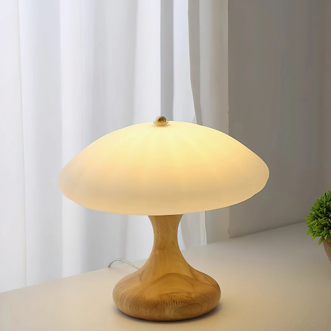 Mushroom table lamp with light natural wood base fully illuminated frosted glass shade, front three-quarter view sheer curtain background