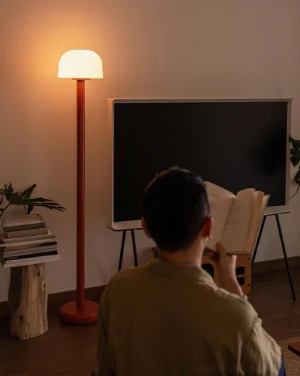 Muto modern floor lamp with warm LED glow in living room reading corner, three-quarter rear angle view with ambient lighting