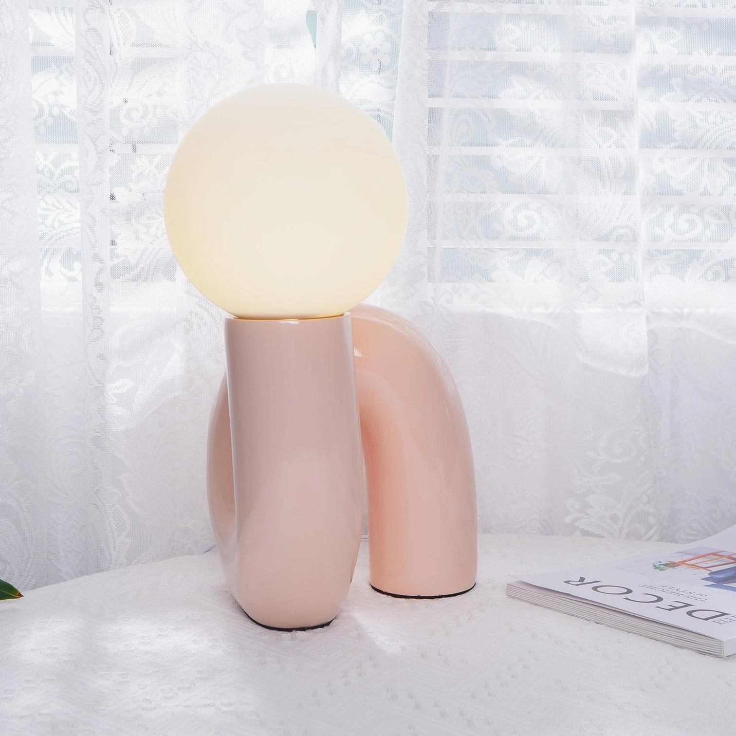 Pink ceramic N-shape table lamp glowing warmly on bedroom windowsill, modern minimalist bedroom decor