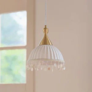 Nacara shell pendant light side angle highlighting brass hardware, fluted porcelain shade, and beaded shell tassel trim in residential interior