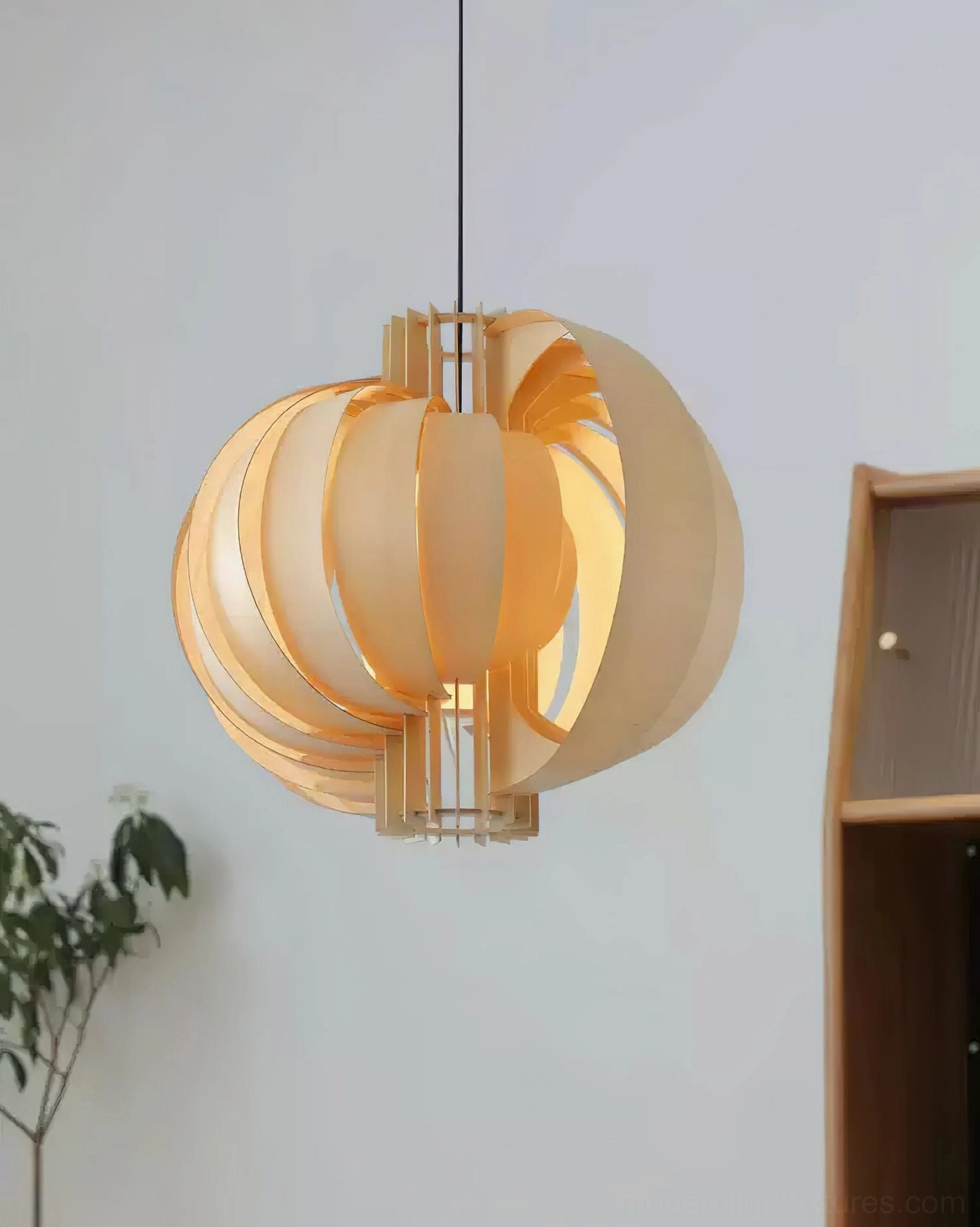 Natural wood toned spherical pendant lamp illuminated in modern interior corner with plant and wooden furniture