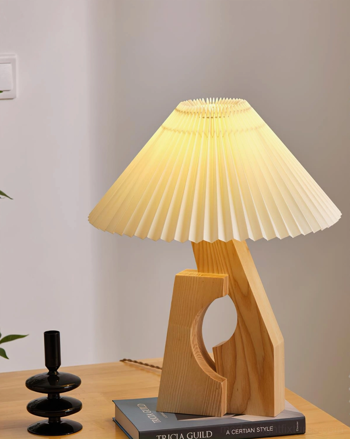 Illuminated pleated table lamp with natural wood base creating warm light, desktop candle holder and book styling