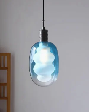 Modern cloud-shaped pendant light installed in Nordic minimalist interior, blue gradient glass with black metal cap above wooden furniture
