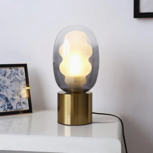 Smoky grey gradient glass Nimbus table lamp displayed on residential side table with botanical wall art, lit bulb creating atmospheric glow