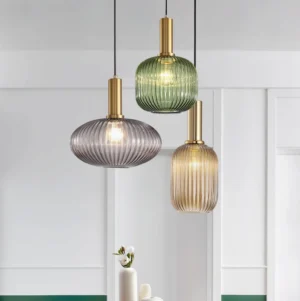Three ribbed glass pendant lights hanging in modern home interior showing green, smoke gray, and cognac finishes in Nordic design setting