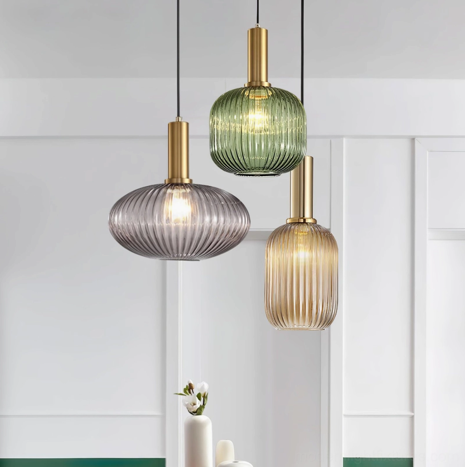 Three ribbed glass pendant lights hanging in modern home interior showing green, smoke gray, and cognac finishes in Nordic design setting