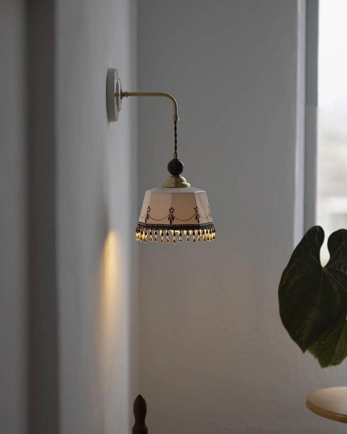 Pink-toned Noemi ceramic wall sconce close-up, tassel fringe detail, brass hardware, ambient warm lighting, indoor window scene