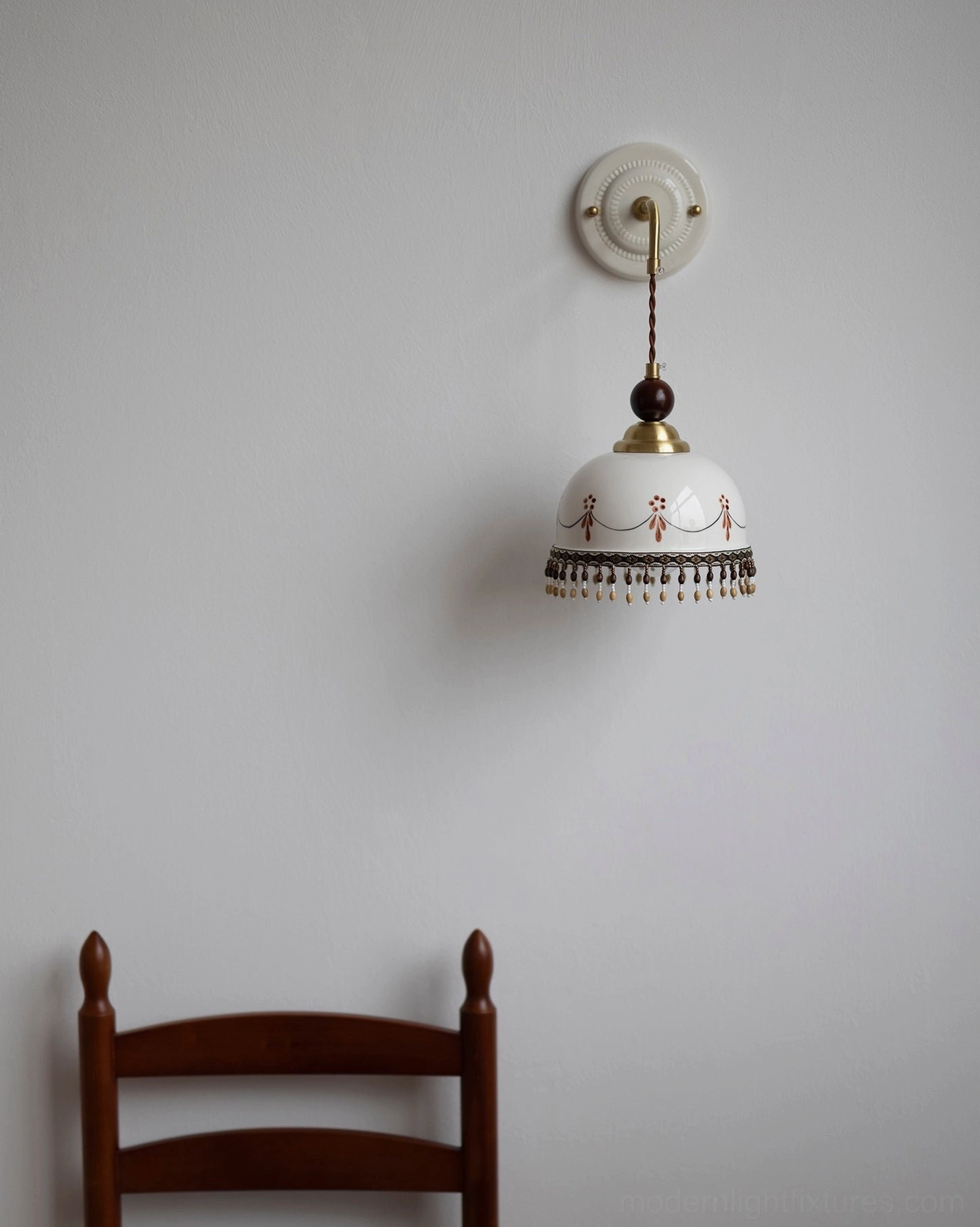 Vintage Noemi ceramic wall lamp frontal view, plain wall with wooden chair, white patterned ceramic shade, artisanal hand-painted