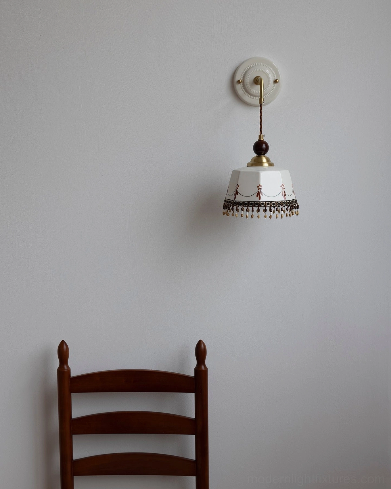 Compact vintage Noemi wall sconce, pinkish ceramic shade with tassel trim and antique brass hardware, frontal studio angle