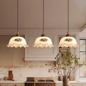 Three matching Nonna floral pendant lights hung over farmhouse kitchen island with neutral wood cabinetry and bar stools