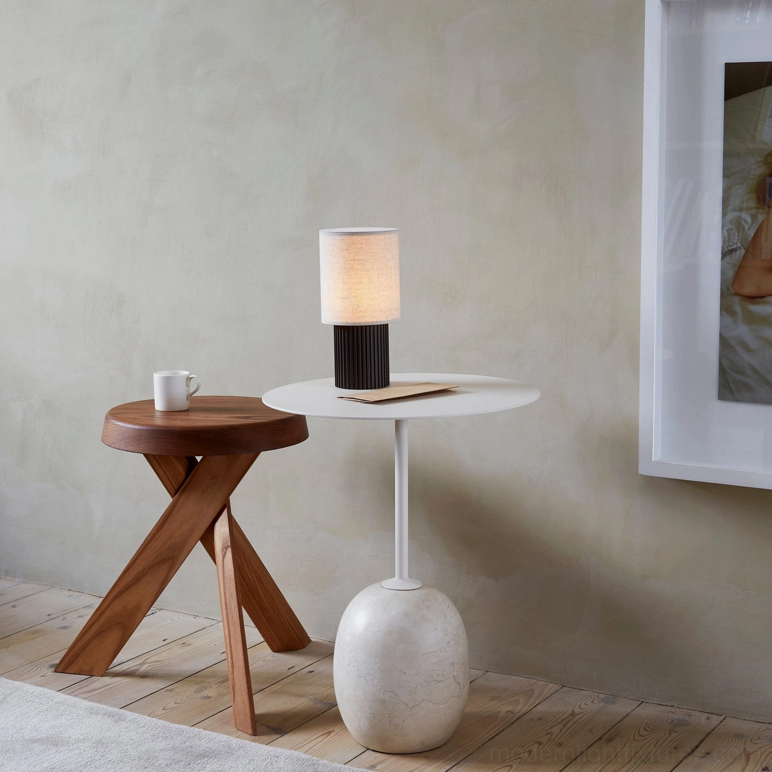 Nordic home setting with contemporary wireless charging table lamp on white round side table, wooden stool accent, three-quarter angle