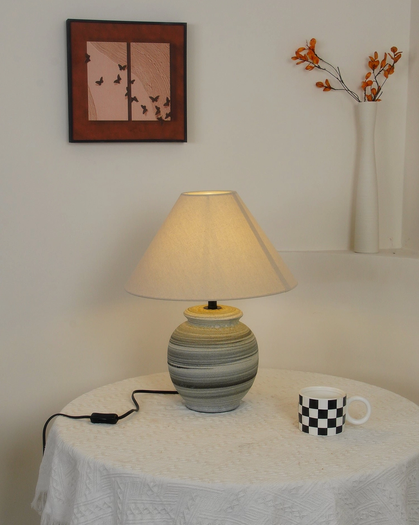 Norma ceramic table lamp on floating shelf showing warm light diffusion through natural linen shade