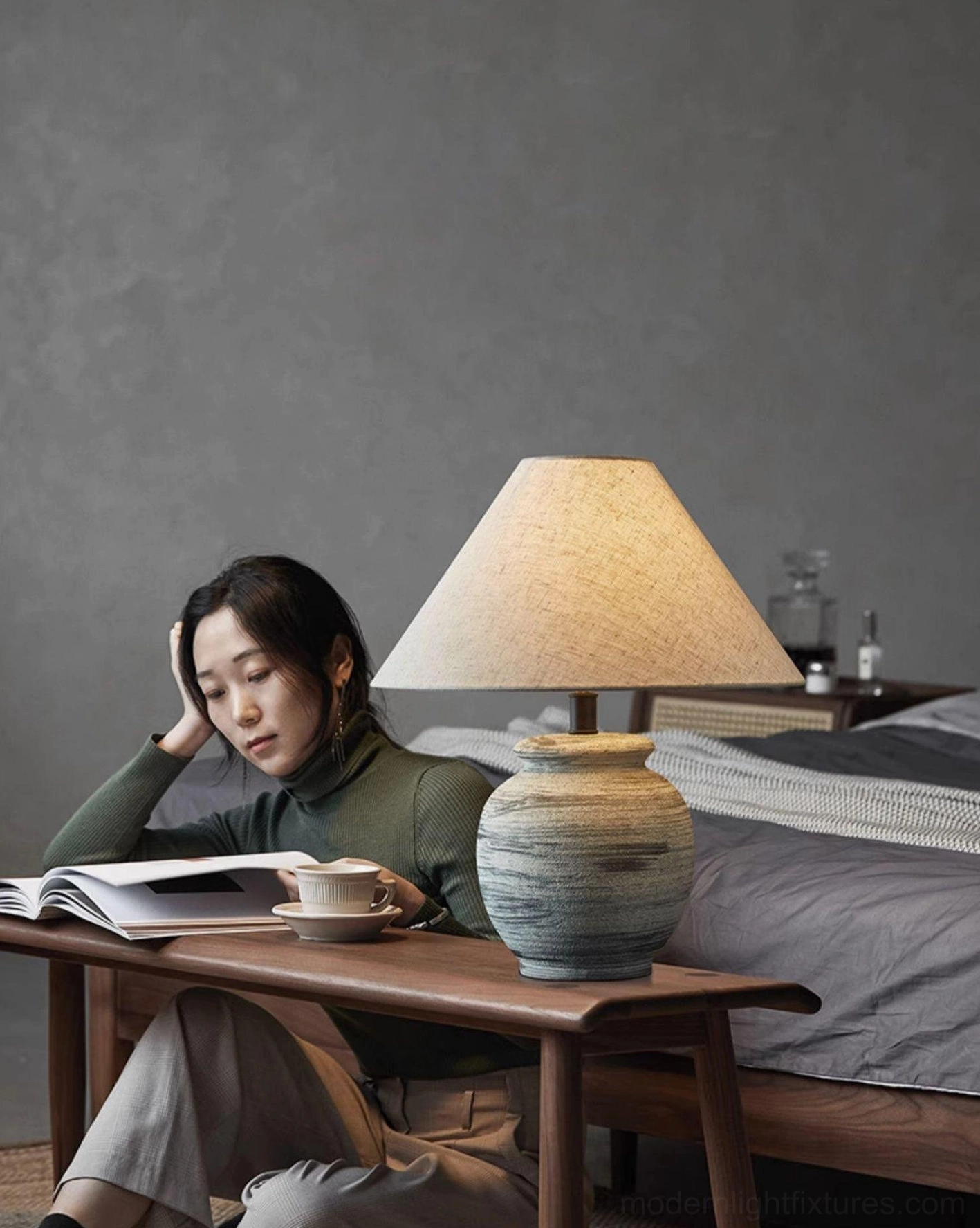 Norma ceramic lamp on wooden desk in bedroom study space with woman reading, soft natural lighting