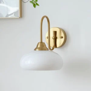 Nova brass wall light sconce three-quarter angle showing curved metal arm and white glass diffuser in home interior