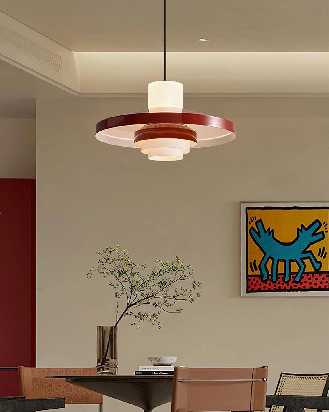 Nova Cap tiered pendant light with wine red shade glowing warm light above modern dining table with wall art