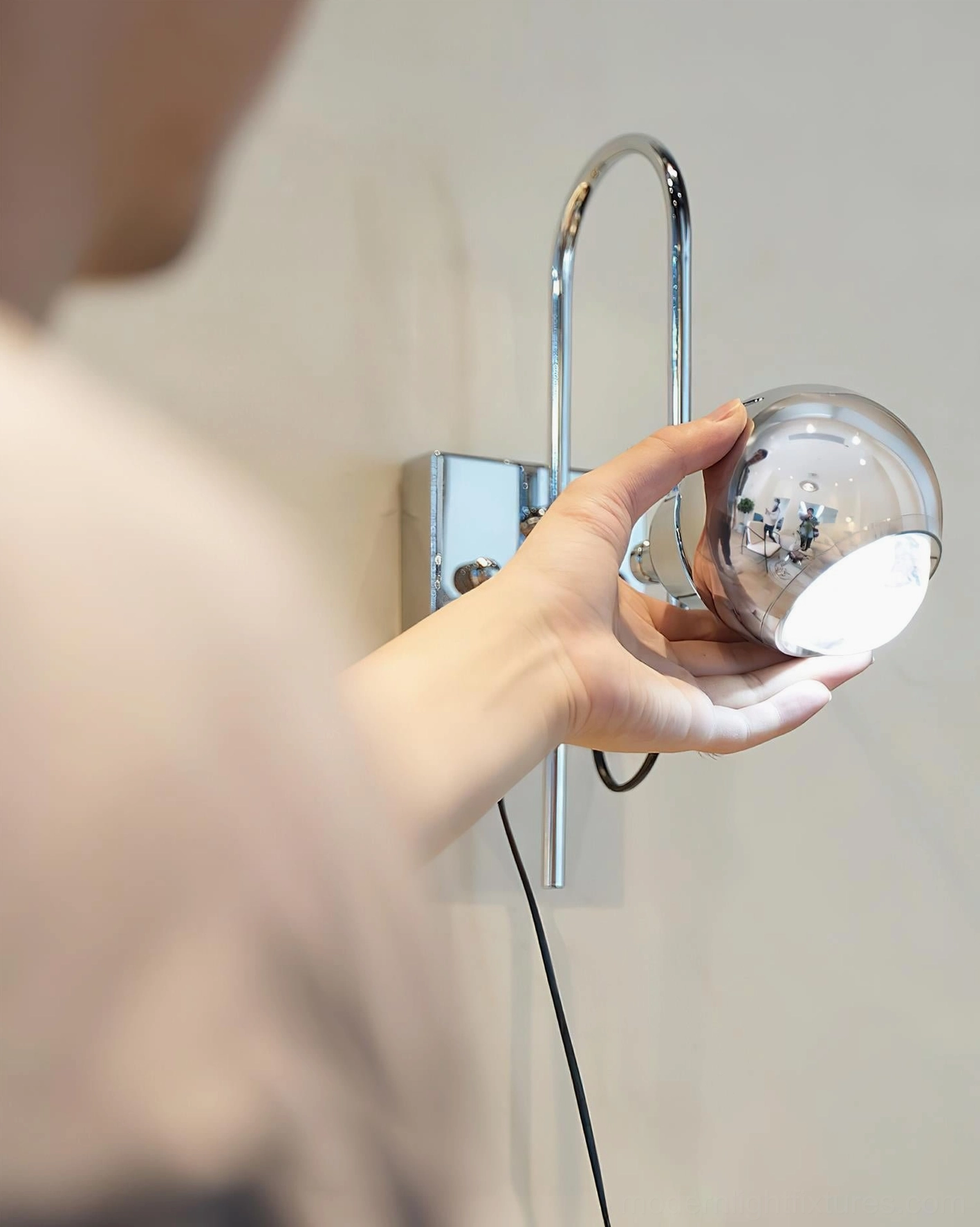 Close-up detail of Nova Dot adjustable wall sconce showing hand rotating the rotatable lamp head with spherical shade
