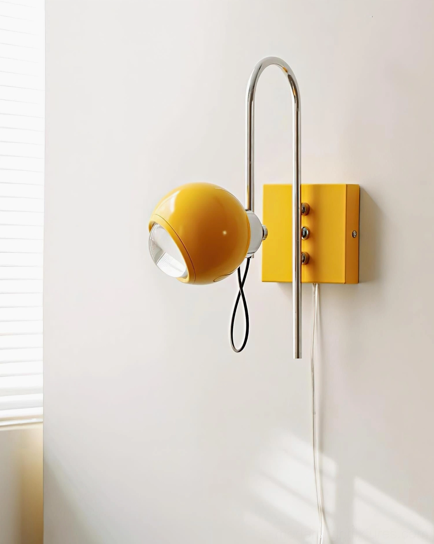 Illuminated Nova Dot yellow wall sconce with lit spherical shade and yellow square wall base mounting, front three-quarter view
