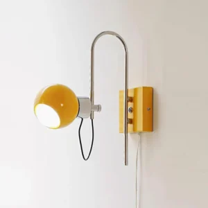 Lit Nova Dot yellow adjustable wall sconce with illuminated spherical shade and exposed power cord, front three-quarter view