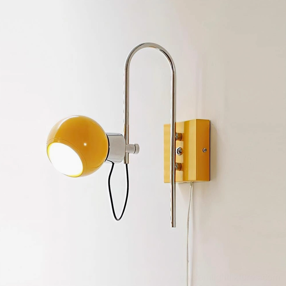 Lit Nova Dot yellow adjustable wall sconce with illuminated spherical shade and exposed power cord, front three-quarter view