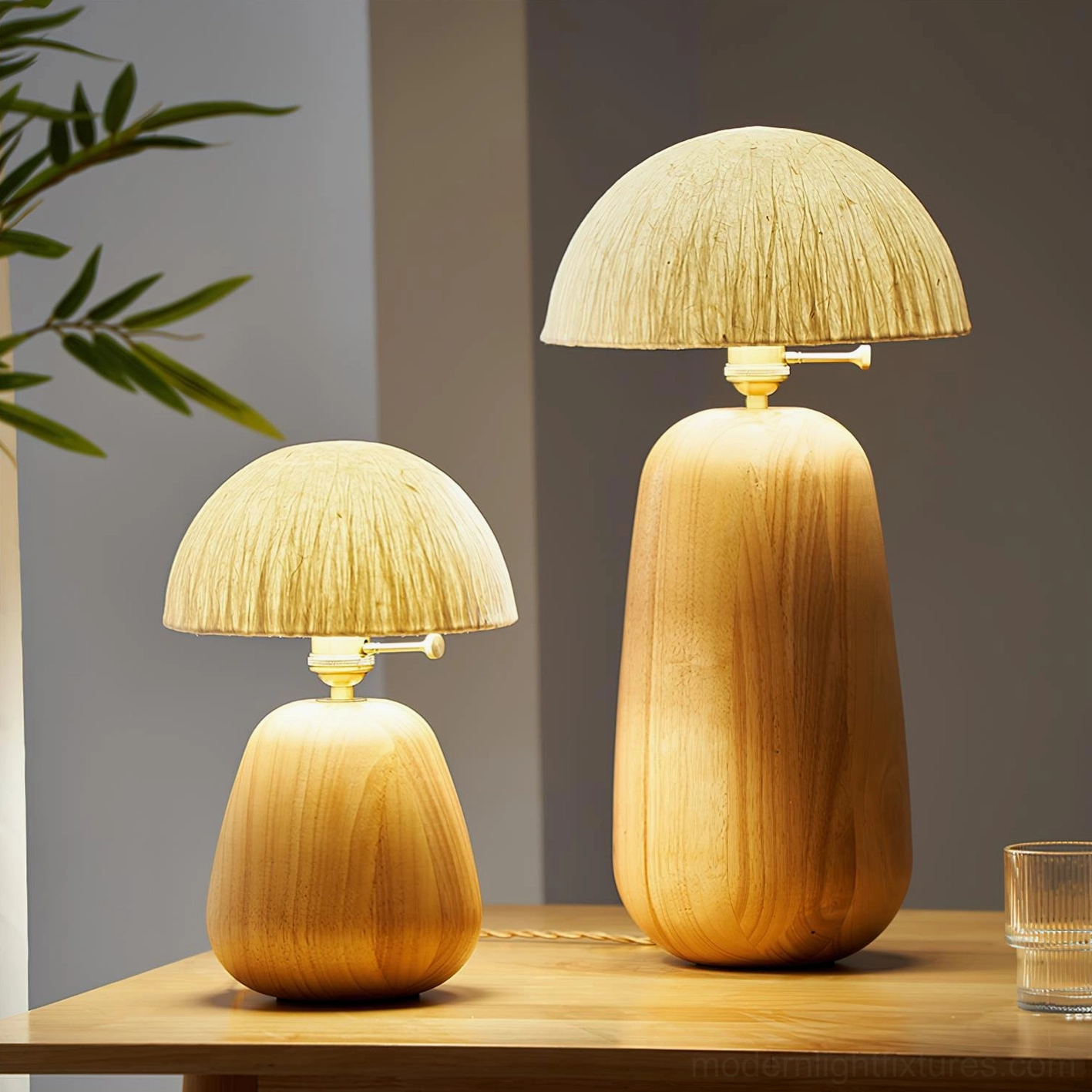 Pair of minimalist oak wood table lamps with warm glowing illumination among green foliage on wooden table