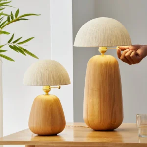 Two sizes of modern oak table lamps with rice paper shades displayed side by side on wooden table with green foliage
