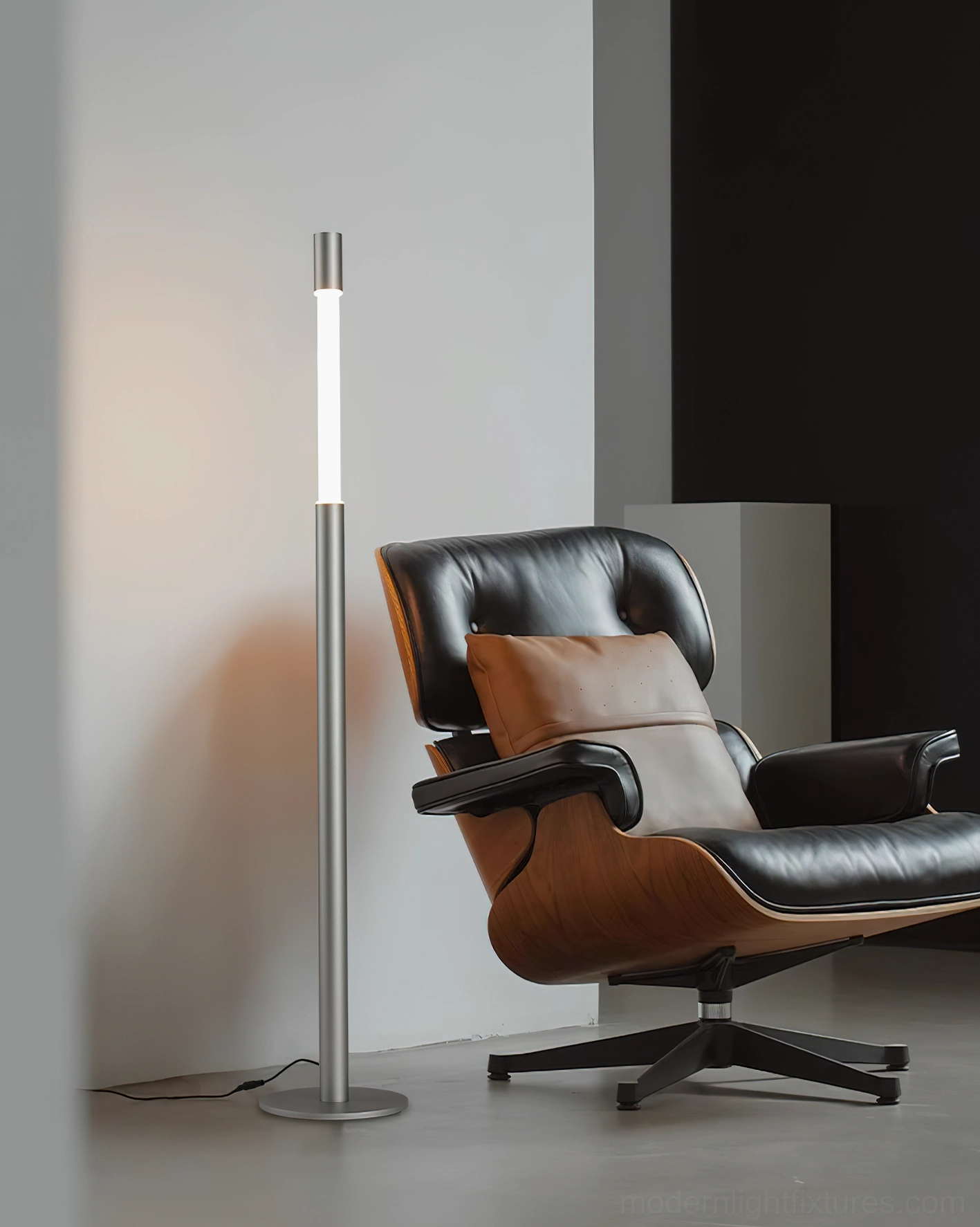 Obelisk brushed silver floor lamp casting warm ambient light in contemporary living room with leather chair