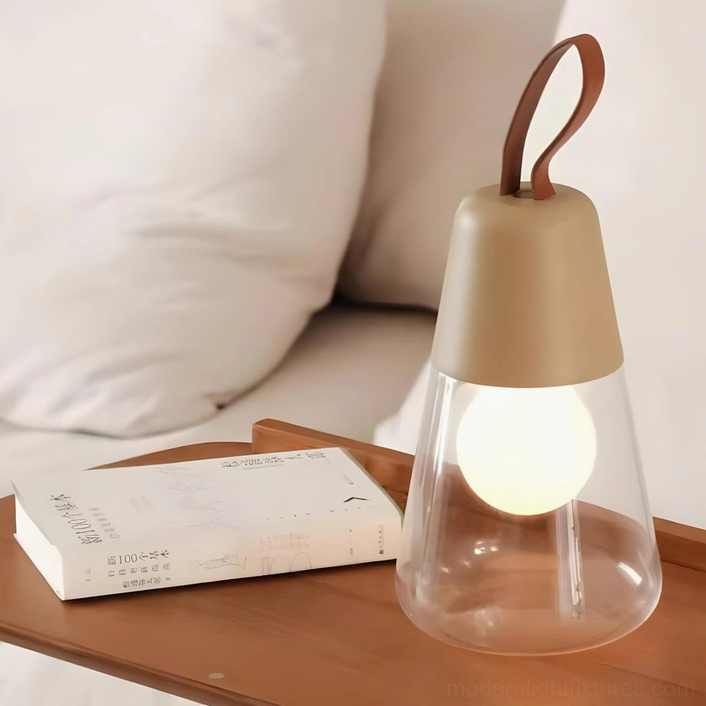 Khaki top Oceana portable table lamp with leather handle placed beside book on wooden bedside nightstand