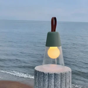 Dark green Oceana portable table lamp with leather strap displayed on coastal beach setting, warm ambient lighting