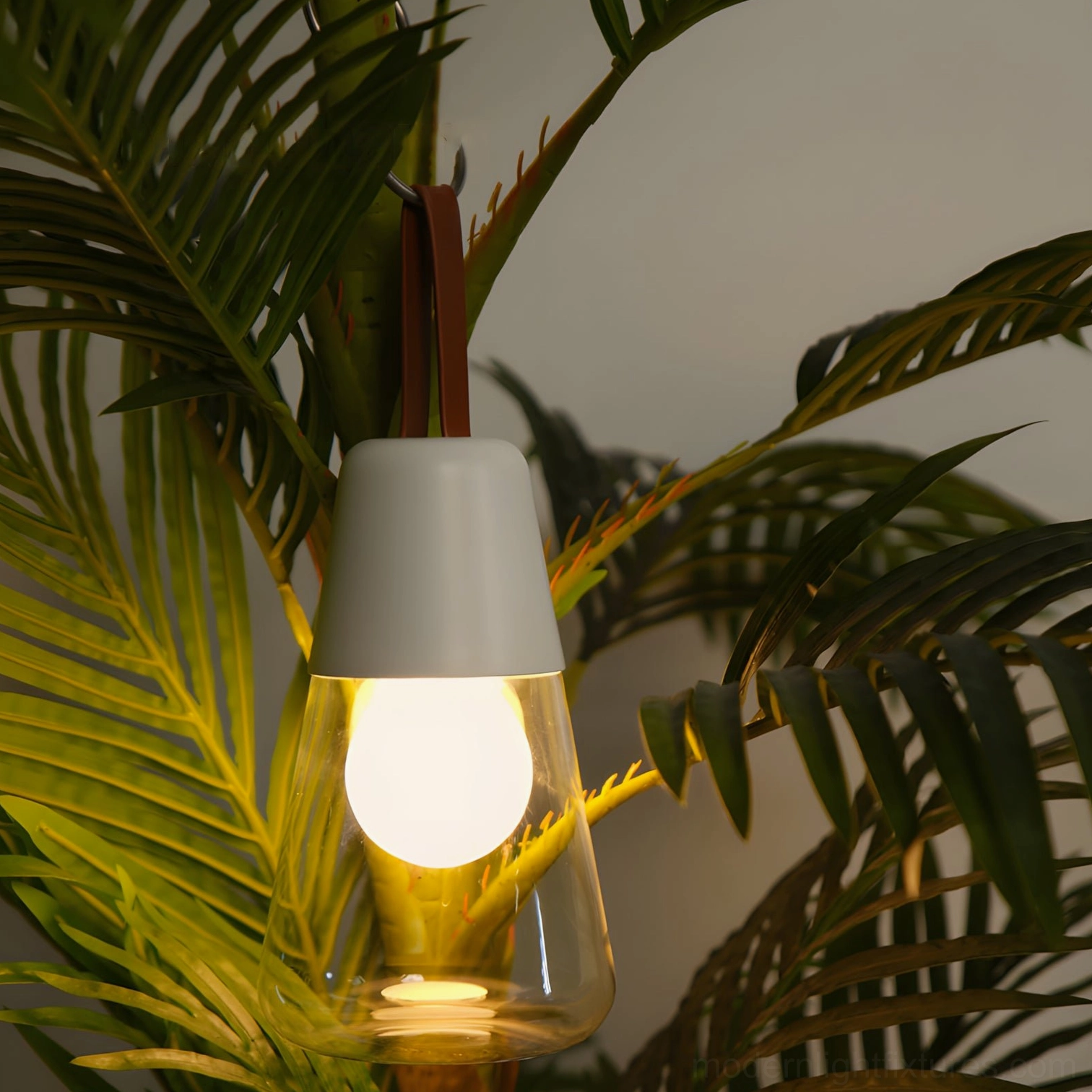 Oceana portable table lamp with light gray top glowing warm light, hung on palm foliage in indoor potted plant area