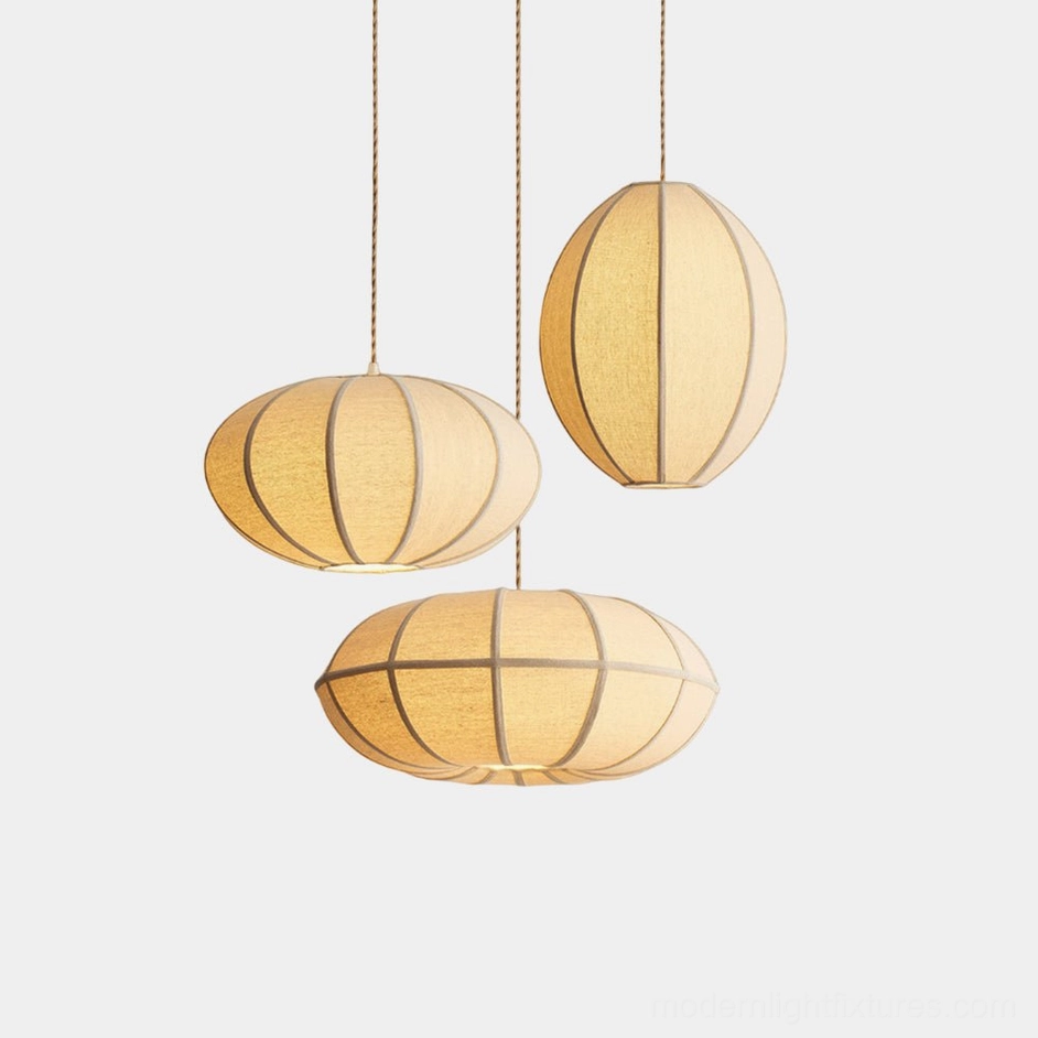 Three Omra modern fabric pendant lights in beige linen with segmented design, overhead studio view on white background, minimalist lantern style fixtures