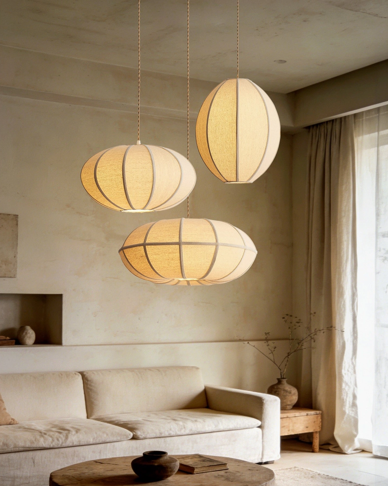 Three Omra oval fabric pendant lamps in neutral tones hanging in cozy residential lounge with warm color palette and woven linen shades