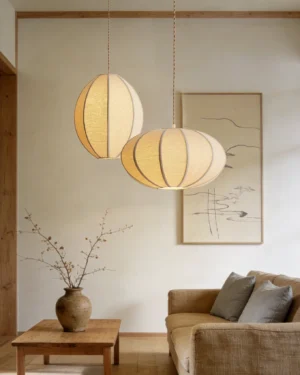 Two Omra pendant lights illuminated in wabi-sabi style living room with sofa and wall art, warm ambient lighting from fabric linen shades