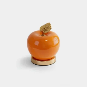 Orange modern apple shaped table lamp with gold metal stem and leaf, front view studio shot with integrated LED warm light