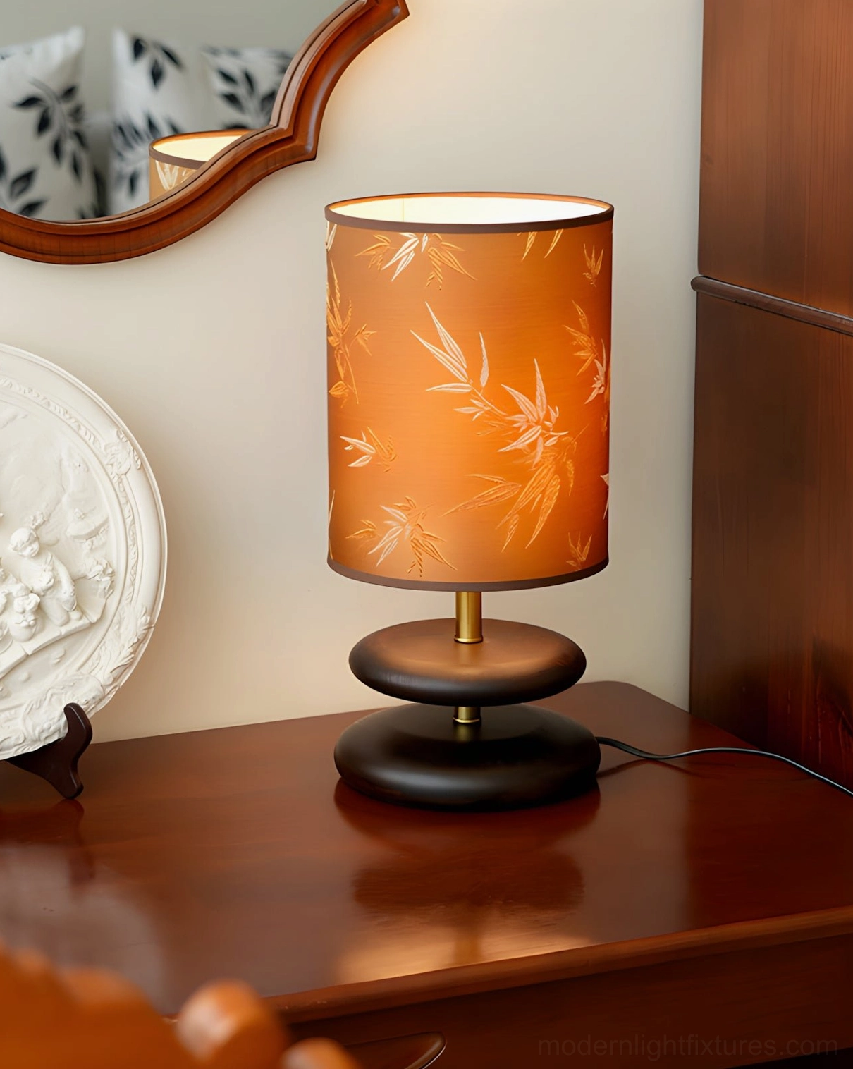 Orange bamboo-leaf print table lamp with dark wood and gold base on wooden side table, three-quarter front view with mirror decor