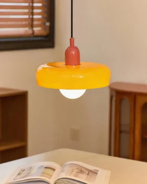 Orange donut pendant light hanging over modern dining table, overhead view showing warm illumination and retro aesthetic in contemporary interior