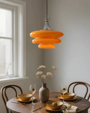 Tiered orange glass pendant light illuminated above round wooden dining table in retro mid-century interior setting