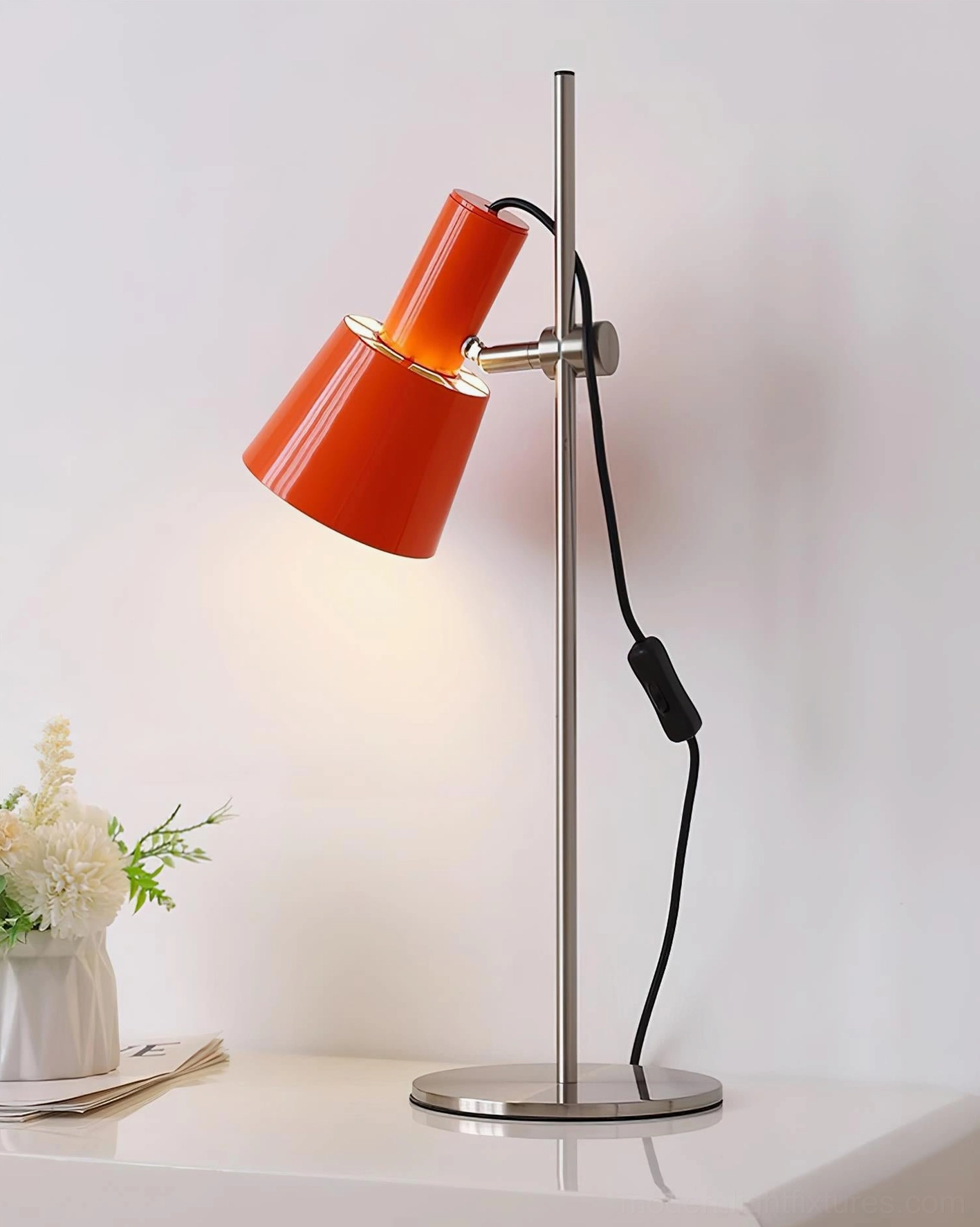 Modern orange-red adjustable table lamp with illuminated shade in three-quarter view with flower decoration