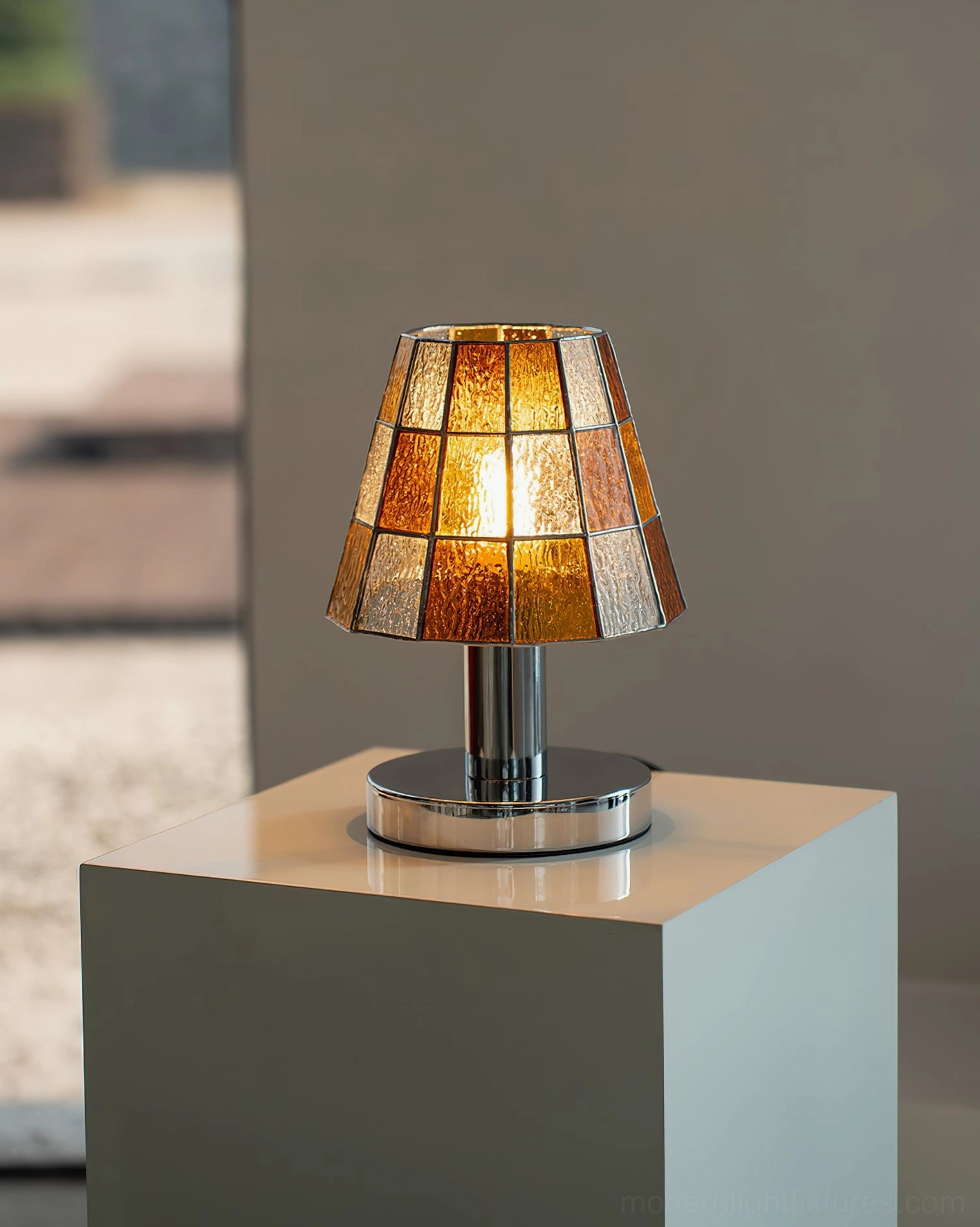 Illuminated orange stained glass geometric lamp with chrome hardware on neutral display backdrop