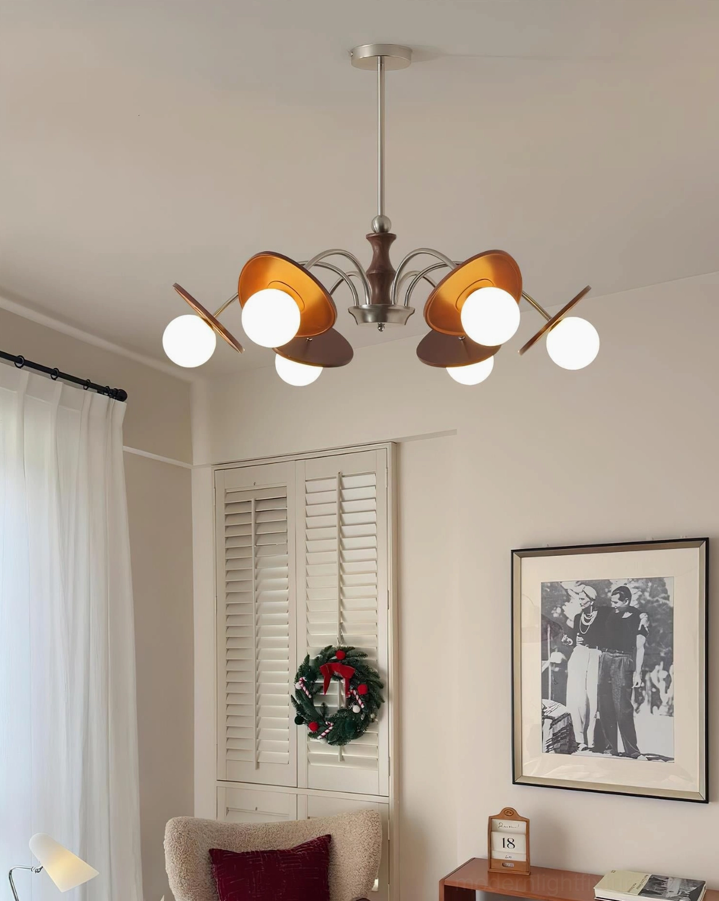 Lit modern orbital chandelier as focal point in cozy neutral-toned lounge room with wall art and window shutters
