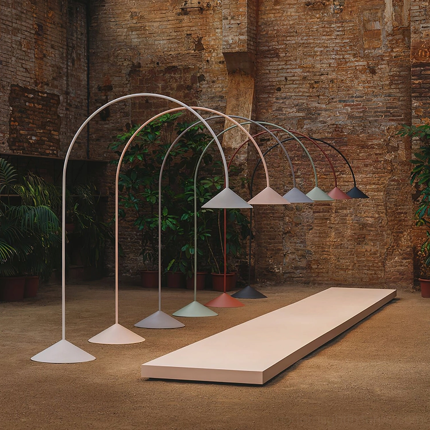Multiple Orbitas arc floor lamps in assorted pastel colors on exposed brick wall outdoor courtyard