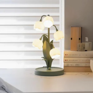 Modern botanical table lamp displayed on indoor nightstand with books and window blinds in background