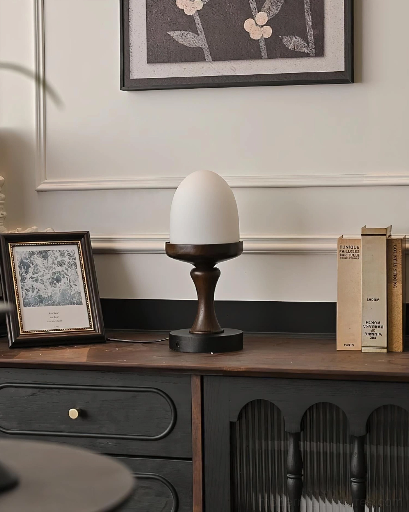 Frosted glass egg-shaped table lamp with wood base on small retro dresser, ambient bedroom lighting